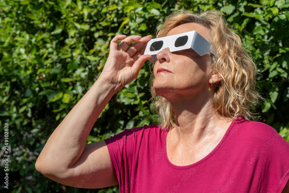 Obraz premium Blonde woman in red observes the sun with classic solar eclipse protective glasses