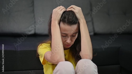 Stressed woman suffering from headache depression and anxiety sitting on the floor holding her head in desperation