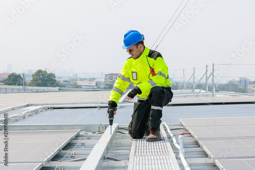 Engineer inspecting solar panel installation on industrial roof Technician in safety vest checking commercial rooftop solar array. Professional worker monitoring green energy solar panels on roof.