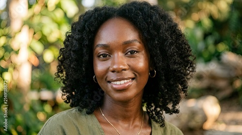 Portrait of a smiling young Black woman with natural curly hair in a sunlit garden setting representing beauty and wellness