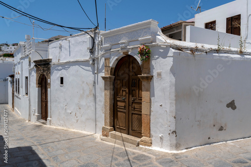 White buildings line a narrow street in Lindos with a clear blue sky on a sunny day in summer