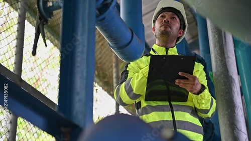 Industrial engineer checking pipeline valves and documenting equipment maintenance work