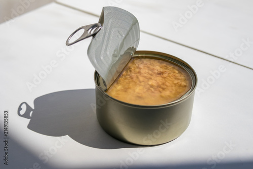 Obraz na plátně Open metal tin can filled with canned meat on a white table in direct sunlight