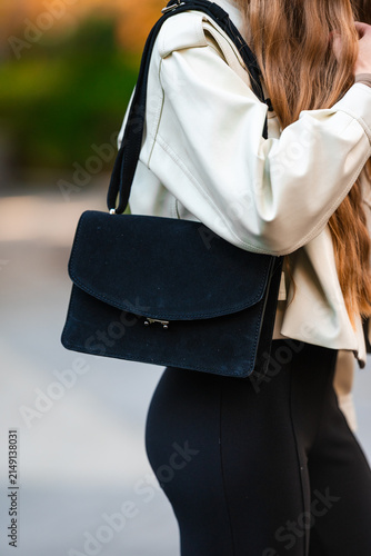 Woman carrying a bag, in outdoor blurred background, with woman, bag, from a side view of woman from behind perspective, with black, white accents, and casual everyday style mood.