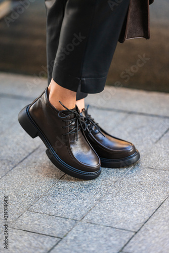 black leather ankle boots standing on urban pavement in casual and stylish fashion setting close-up of feet with gray trousers and clean background copy space for editorial use.