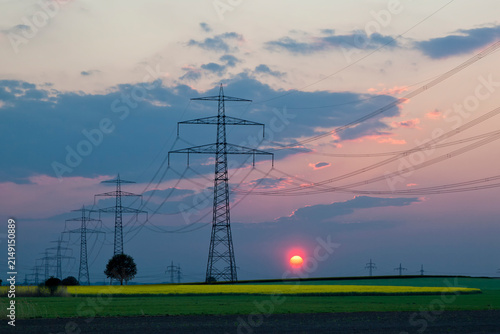 Germany, Bavaria, View of electricity pylon in rapeseed field at sunset