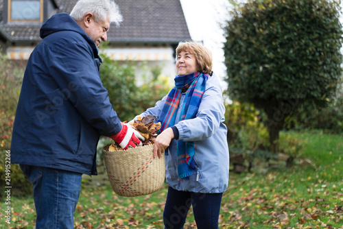 A couple collects autumn leaves in a garden basket outdoors