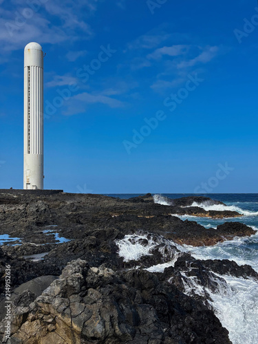 Punta del Hidalgo Lighthouse rising above rugged volcanic rocks on the Atlantic coast of Tenerife, Canary Islands, Spain. A striking coastal landscape with crashing waves and basalt formations