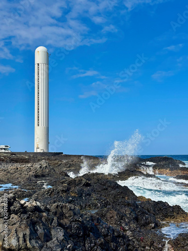 Punta del Hidalgo Lighthouse rising above rugged volcanic rocks on the Atlantic coast of Tenerife, Canary Islands, Spain. A striking coastal landscape with crashing waves and basalt formations
