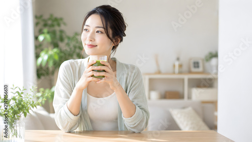 明るい部屋でグリーンスムージーを手に穏やかな笑顔を見せる若い女性