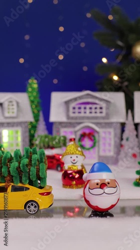 Against the backdrop of a Christmas village in the foreground is an unusual Santa Claus and a yellow car