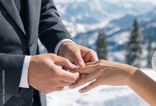Groom putting a diamond engagement ring on his bridefinger during a winter outdoor wedding ceremony