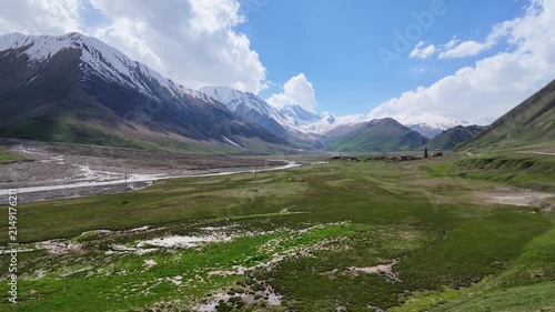 Panoramic view of majestic mountain range with snowy peaks, sprawling green valley, flowing river, traditional rural village houses, summer scenery, adventure travel, Truso valley, Georgia