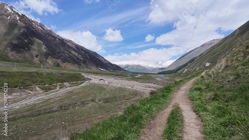 Panoramic view of a rugged Truso valley, Georgia with a winding dirt road and grassy hills, showcasing alpine landscape, hiking trails, wilderness adventure, and majestic nature scenery
