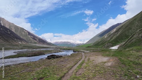 scenic mountain at Truso valley, Georgia with flowing river stream, melting snow peaks, lush green meadows, cloudy blue sky, perfect for travel, adventure, documentary background footage,