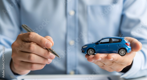 A professional insurance agent holding a miniature blue car model and a pen to signify a new vehicle purchase agreement or auto protection policy