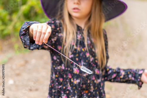 Fotografie little sorceress performing magic ritual with crystal pendulum in magic forest,