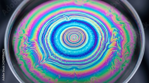 Top view macro close up of soap bubble liquid film surface showing mesmerizing concentric colorful rings created by thin film interference against dark background.