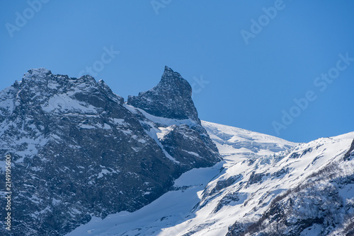 Majestic snow-capped mountain peak stands tall against clear blue sky, showcasing rugged beauty of winter landscape. Karachay-Cherkessia. Dombay 2025. Nature concept for design.