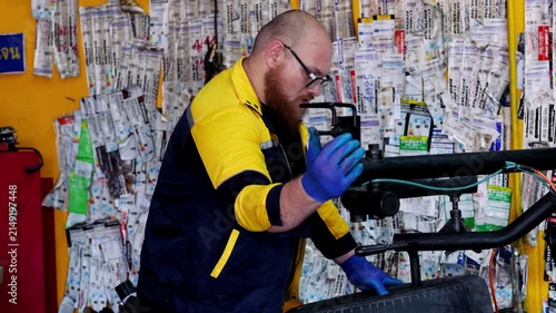 Skilled professional mechanic focused on repairing automotive tire wheel inside modern garage workshop with serious expression and diligent work ethic