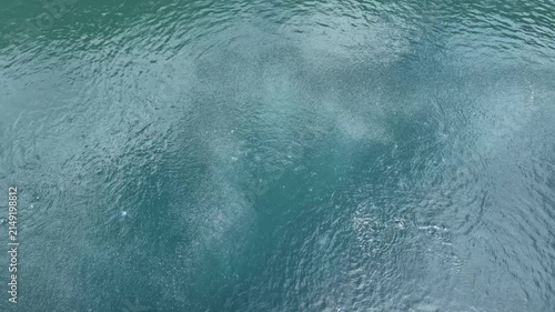 Clear turquoise water surface with gentle ripples and tiny bubbles rising, perfect for background texture, tranquil nature scene