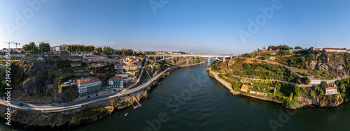 Aerial view of the Ponte Infante Dom Henrique bridge spanning the Douro River, connecting the historic urban landscape with lush green hillsides in Vila Nova de Gaia, Porto, Portugal.