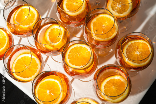 Flat lay of repeated rows of cold summer alcohol aperitif cocktails with juicy orange slices under bright sunlight