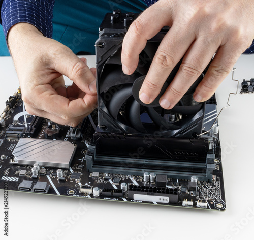 the hands of a man installing a fan on the CPU cooler tower on the motherboard close-up front view