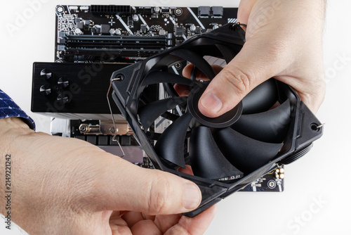 the hands of a man installing a fan on the CPU cooler tower on the motherboard close-up top view