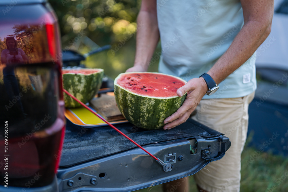 Obraz premium Man holding refreshing watermelon on truck tailgate during summer camping