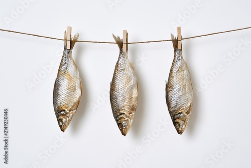 Three dried fish hanging on a clothesline with wooden pegs