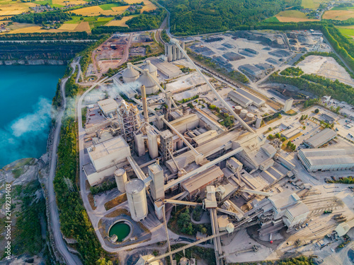 Aerial view of CCB Granulats Gaurain cement plant featuring large silos, conveyor systems, and a turquoise quarry lake surrounded by lush greenery in Tournai, Wallonia, Belgium.