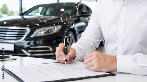 Man signing contract papers at car dealership with salesperson.