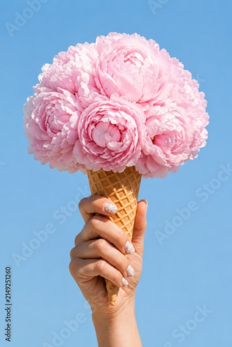 Pink peony flowers in waffle cone held by hand against blue sky