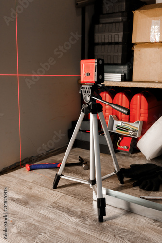 Bild auf Leinwand Red laser level tool on tripod projecting cross lines on wall inside workshop ve