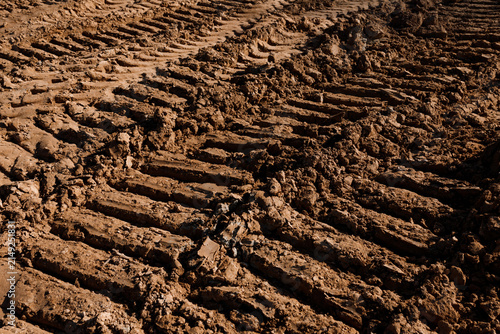 Heavy industrial tire tracks and crawler protector tread marks on wet muddy soil earth background at construction site field countryside dirt road agriculture landscape texture nobody closeup