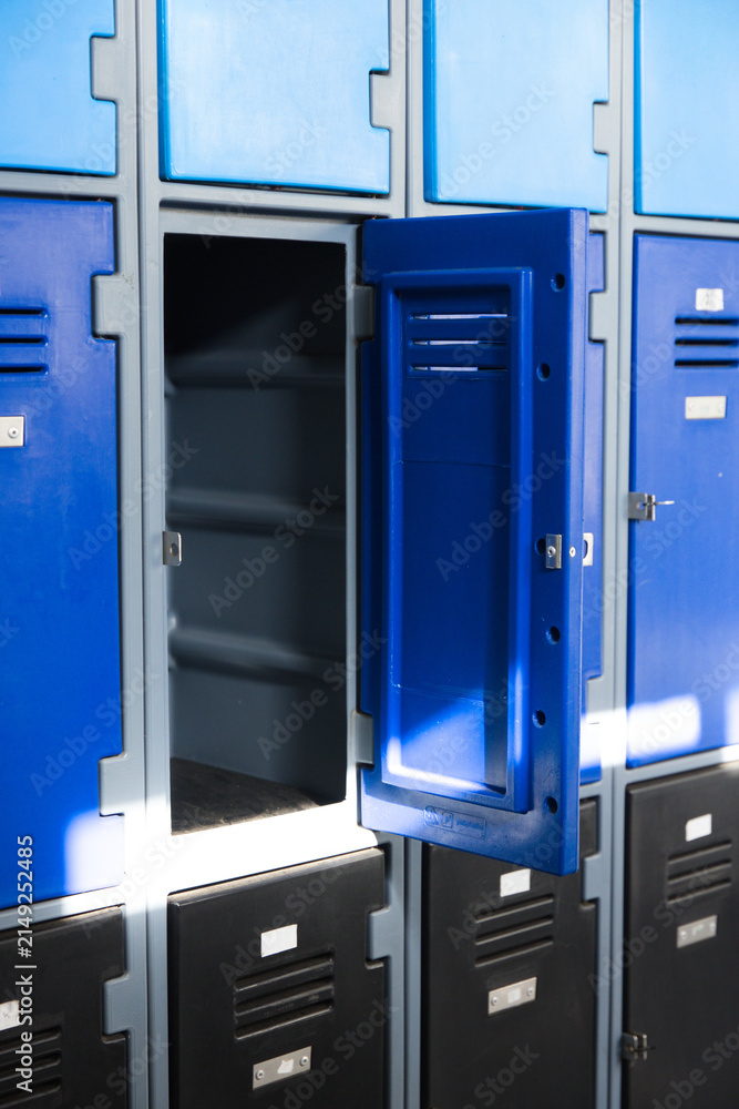 Fototapeta premium Open blue upper locker is revealing empty shelves on hall wall, with sunlight showing scuff marks