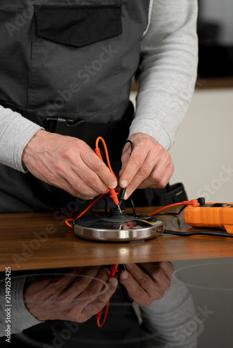 Professional Appliance Repair Technician Testing Electric Cooktop Heating Element with Digital Multimeter During Maintenance