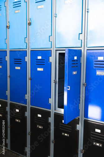 Middle-row blue locker door is standing ajar in metal locker bank, revealing empty shelves, padlock