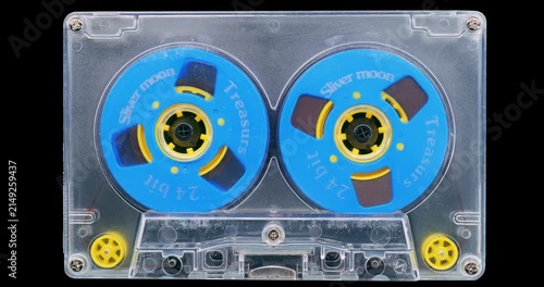 Transparent Audio Cassette with Blue Reels. Front view of a vintage cassette with bright blue reels spinning on a black background.