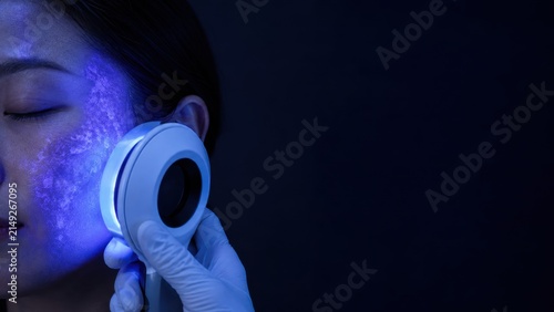 Close-up of woman skin analysis with blue light device by professional wearing glove in dark room
