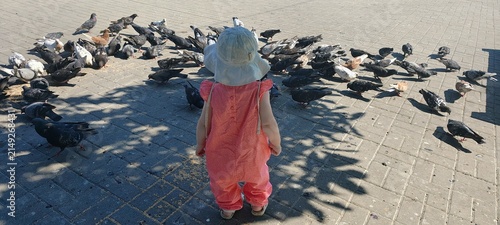 High angle view of toddler child surrounded by flock of pigeons on city square