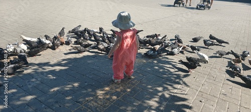 High angle view of toddler child surrounded by flock of pigeons on city square