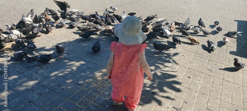 High angle view of toddler child surrounded by flock of pigeons on city square