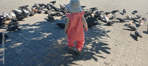 High angle view of toddler child surrounded by flock of pigeons on city square
