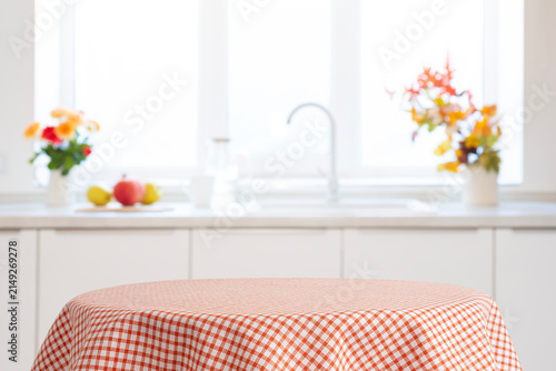 Red checkered tablecloth on table as empty design space of blurred kitchen interior