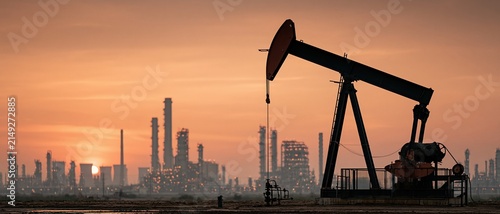 Raw industrial power meets golden hour drama an oil pump jack silhouette dominates the foreground as a vast refinery complex glows against a fiery orange sunset sky.