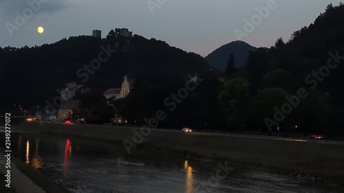 Full moon over the scenic Celje river embankment promenade with evening traffic and calm atmosphere