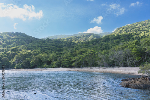Pristine tropical bay on Con Dao Island, Vietnam, featuring a quiet sandy shoreline backed by lush forest hills under a sunny sky.