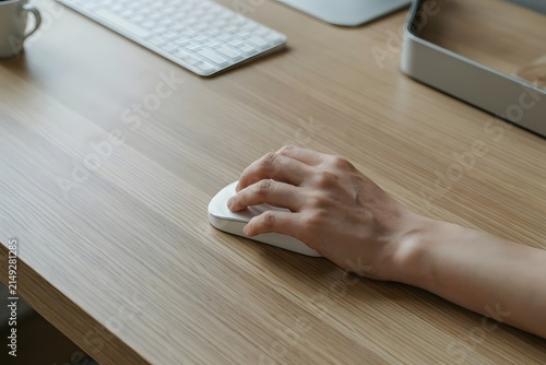 Hand holding a mouse on a desk, with a computer keyboard